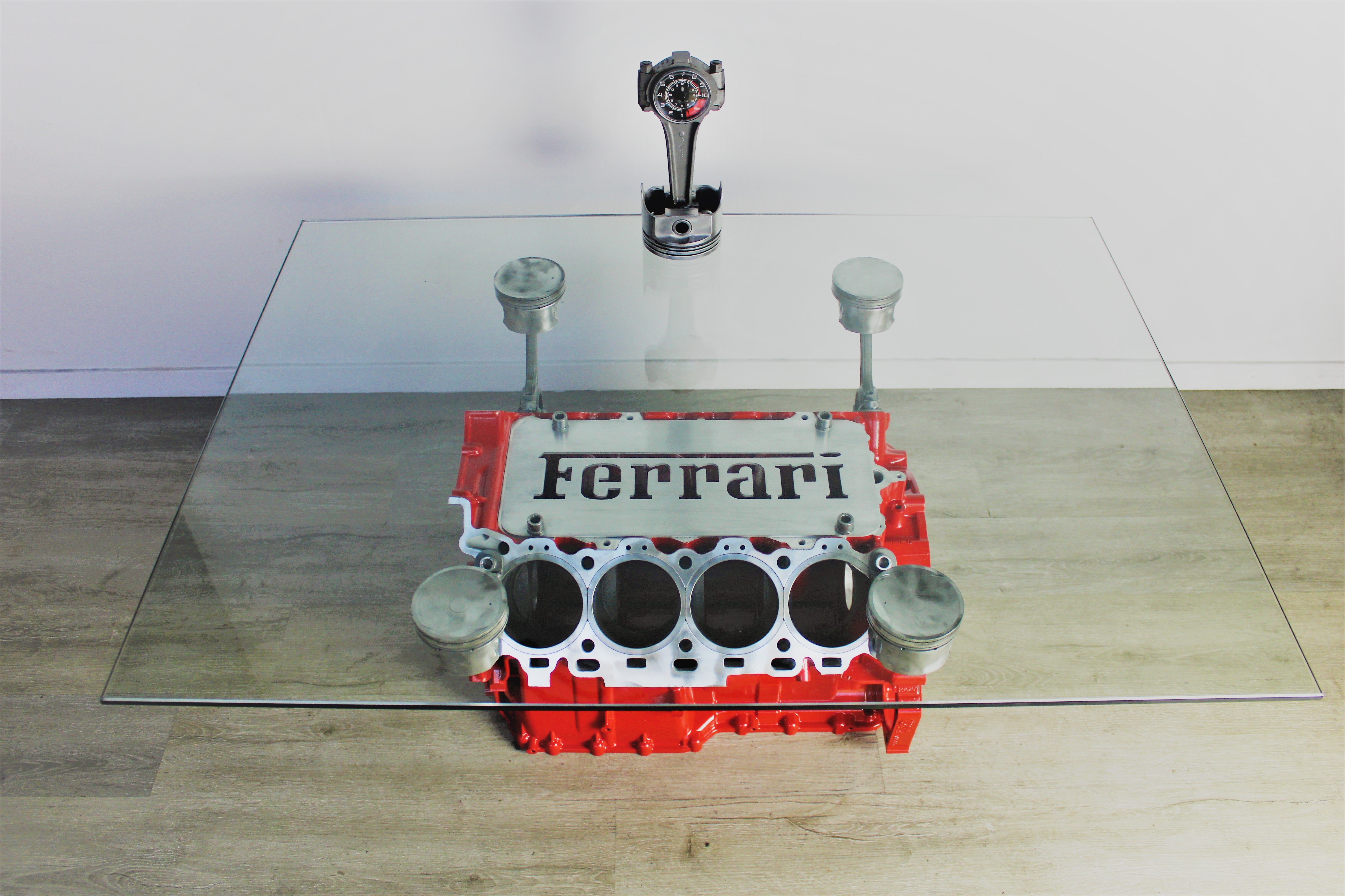 Ferrari engine block coffee table finished in red with a square glass top, the Ferrari logo displayed in the center and a car piston clock on top.