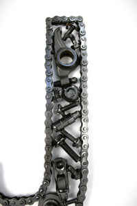 Close-up view of a letter J made out of real car parts, outlined with a timing chain.