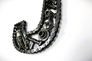 Close-up view of a letter J made out of real car parts, outlined with a timing chain.