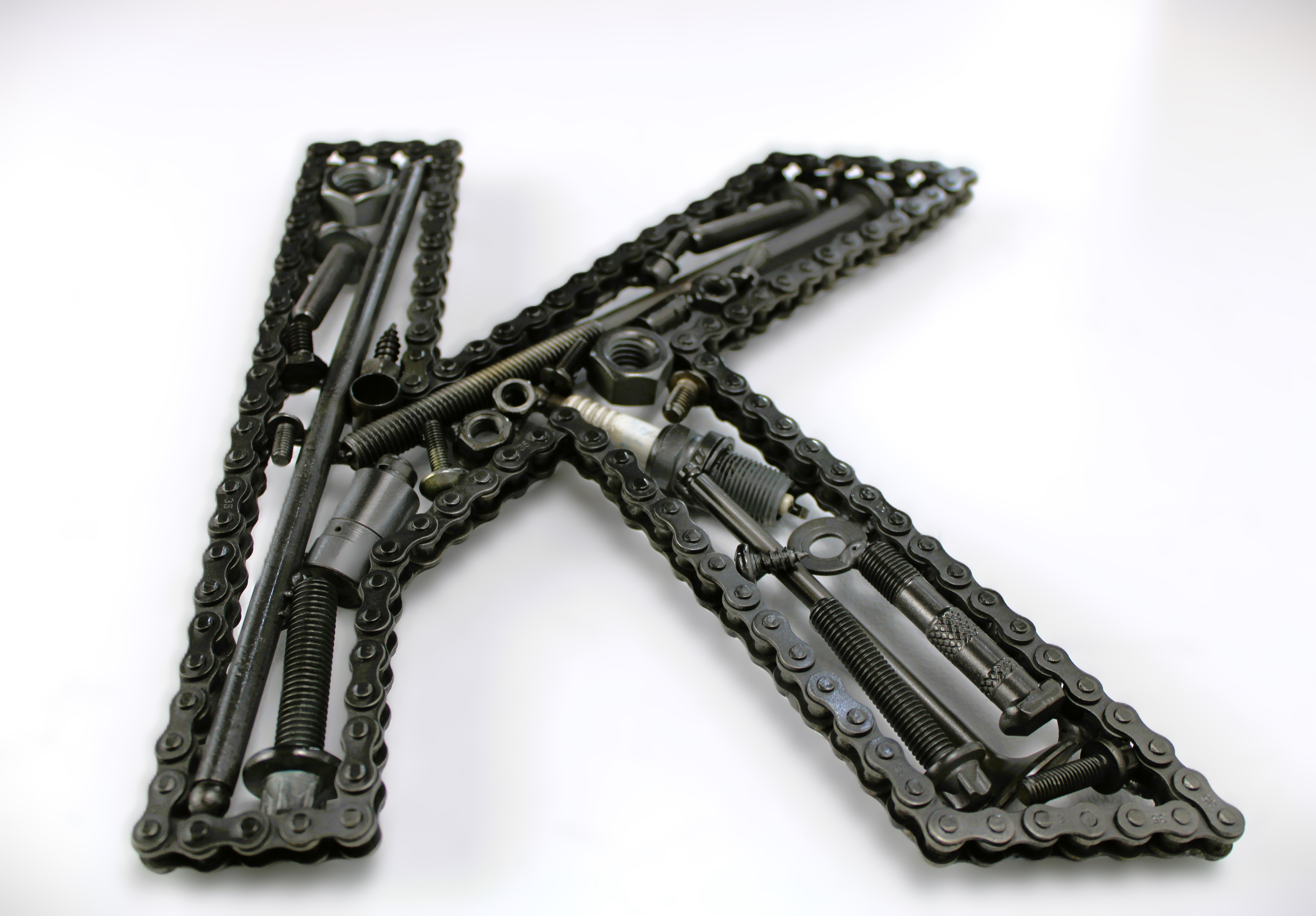 Close-up view of a letter K made out of real car parts, outlined with a timing chain.