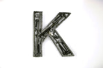 Load image into Gallery viewer, A letter K made out of real car parts, outlined with a timing chain.
