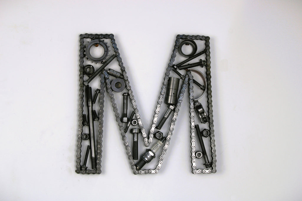 A letter M made out of real car parts, outlined with a timing chain.