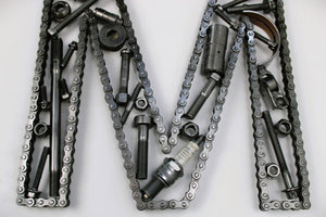 Close-up view of a letter M made out of real car parts, outlined with a timing chain.