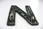 Load image into Gallery viewer, A letter N made out of real car parts, outlined with a timing chain.
