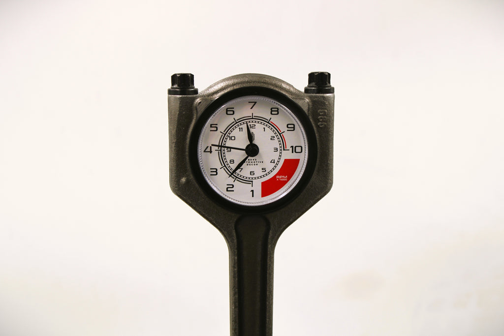 Close-up view of a polished car piston clock with a black clock ring and white and red RPM clock face.