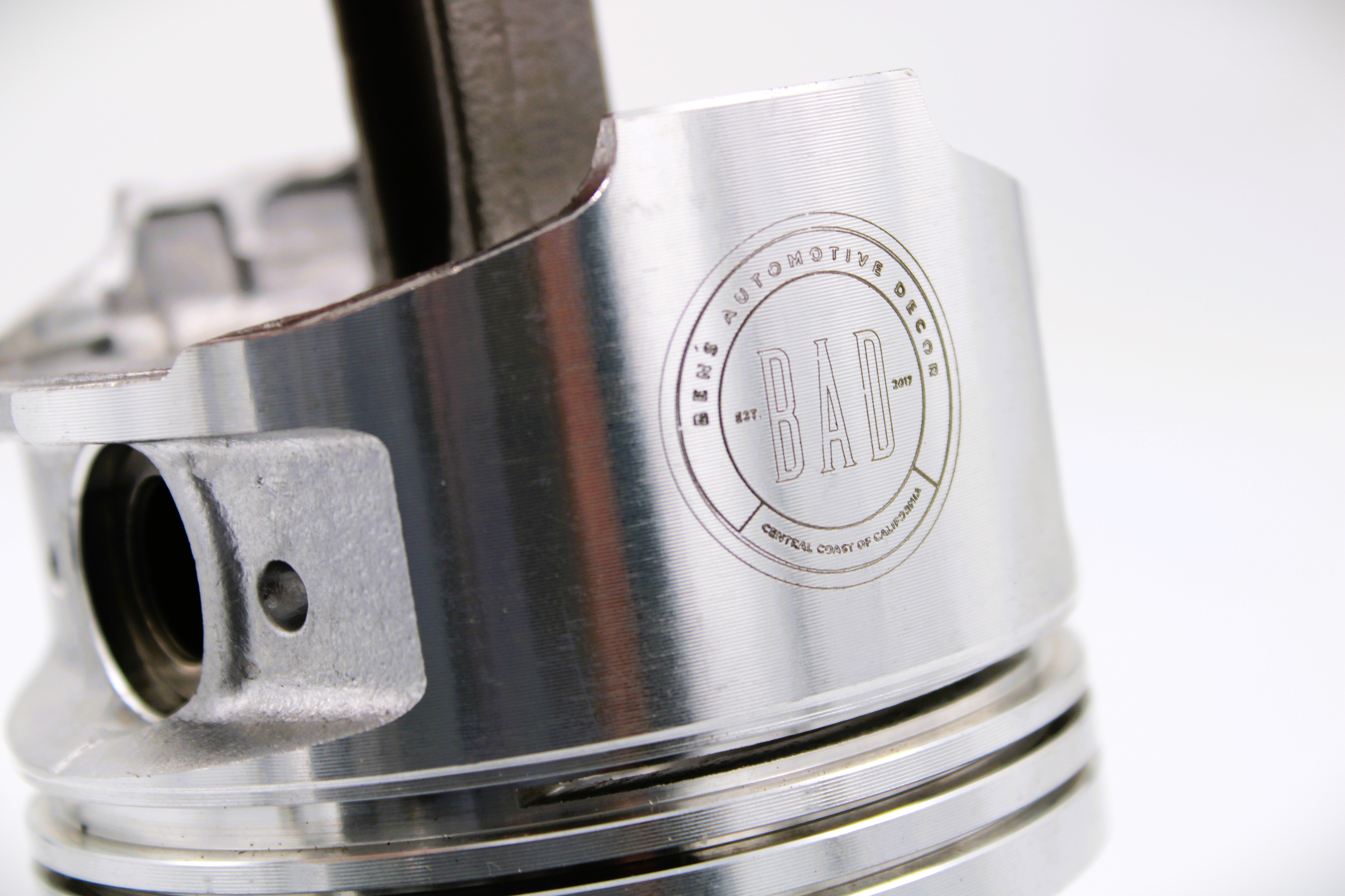 Close-up view of the base of a polished car piston clock, engraved with the Ben's Automotive Decor logo.