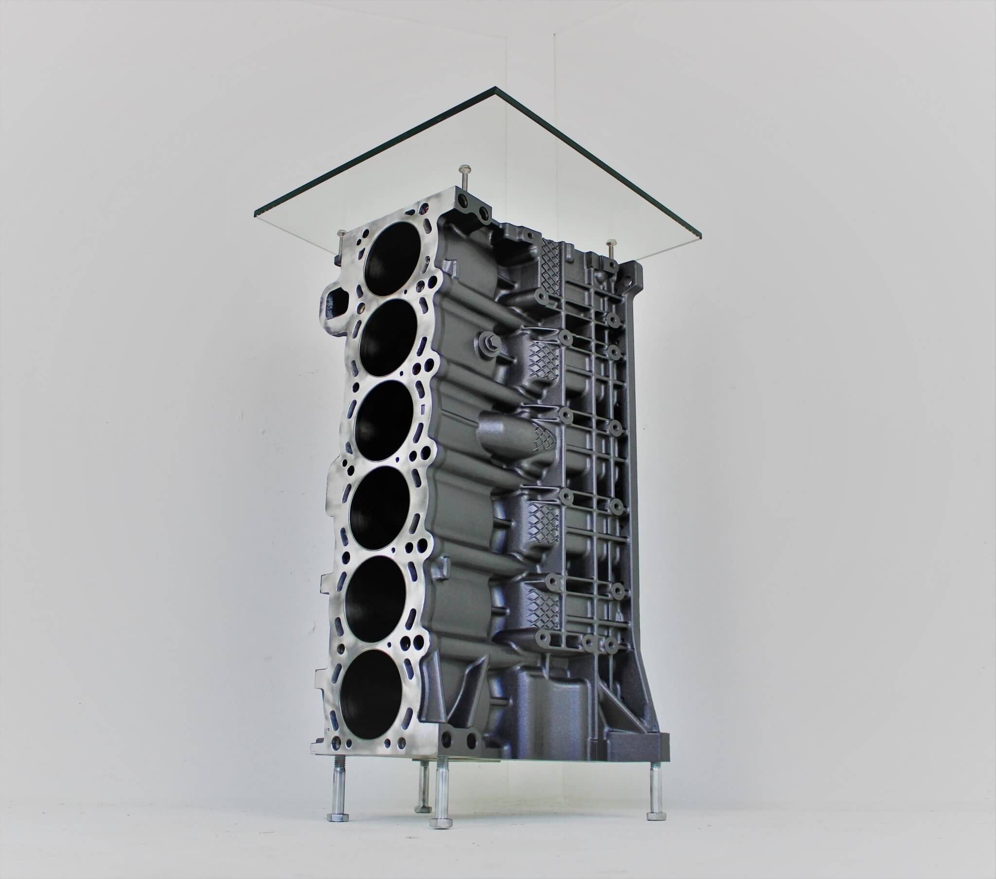 Wine rack table handcrafted from a genuine BMW car engine block finished in gray and silver with a square glass top.