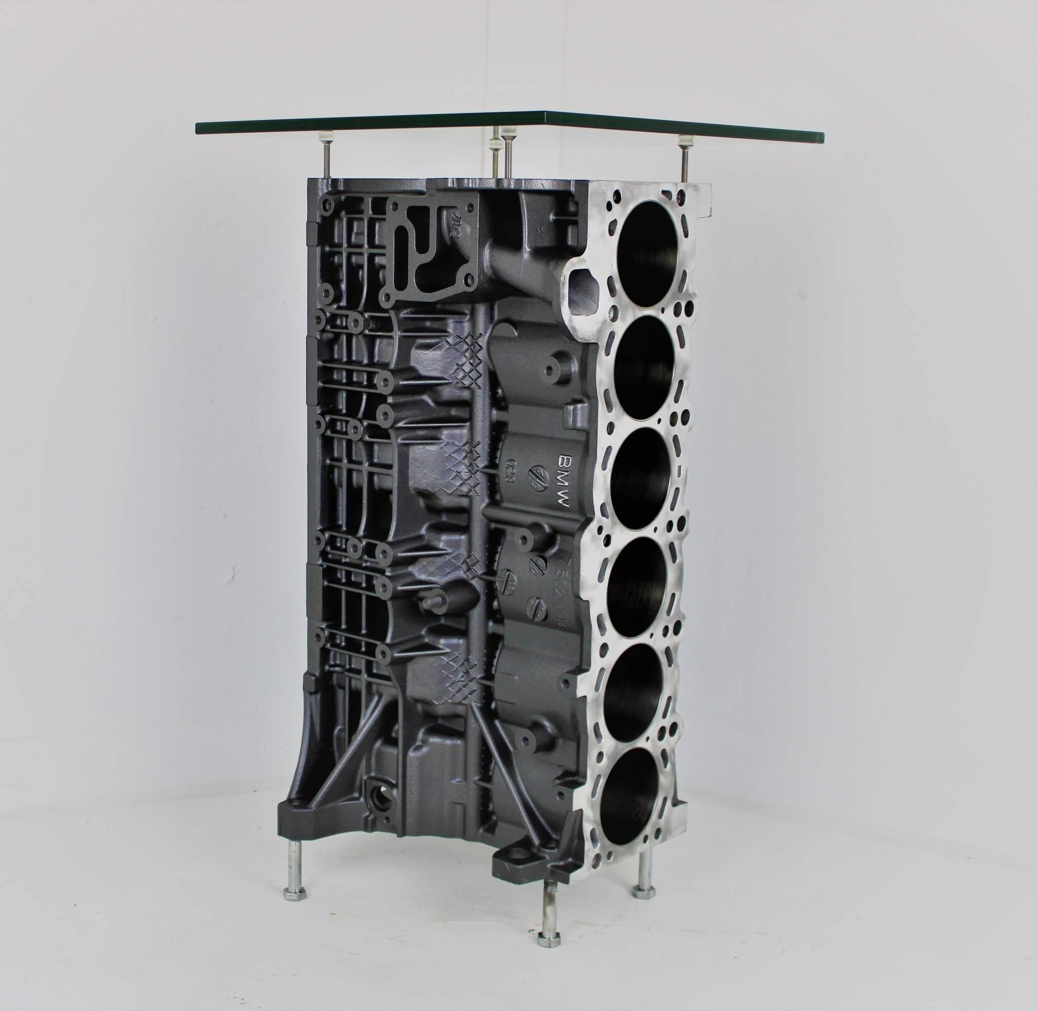 Wine rack table handcrafted from a genuine BMW car engine block finished in gray and silver with a square glass top.
