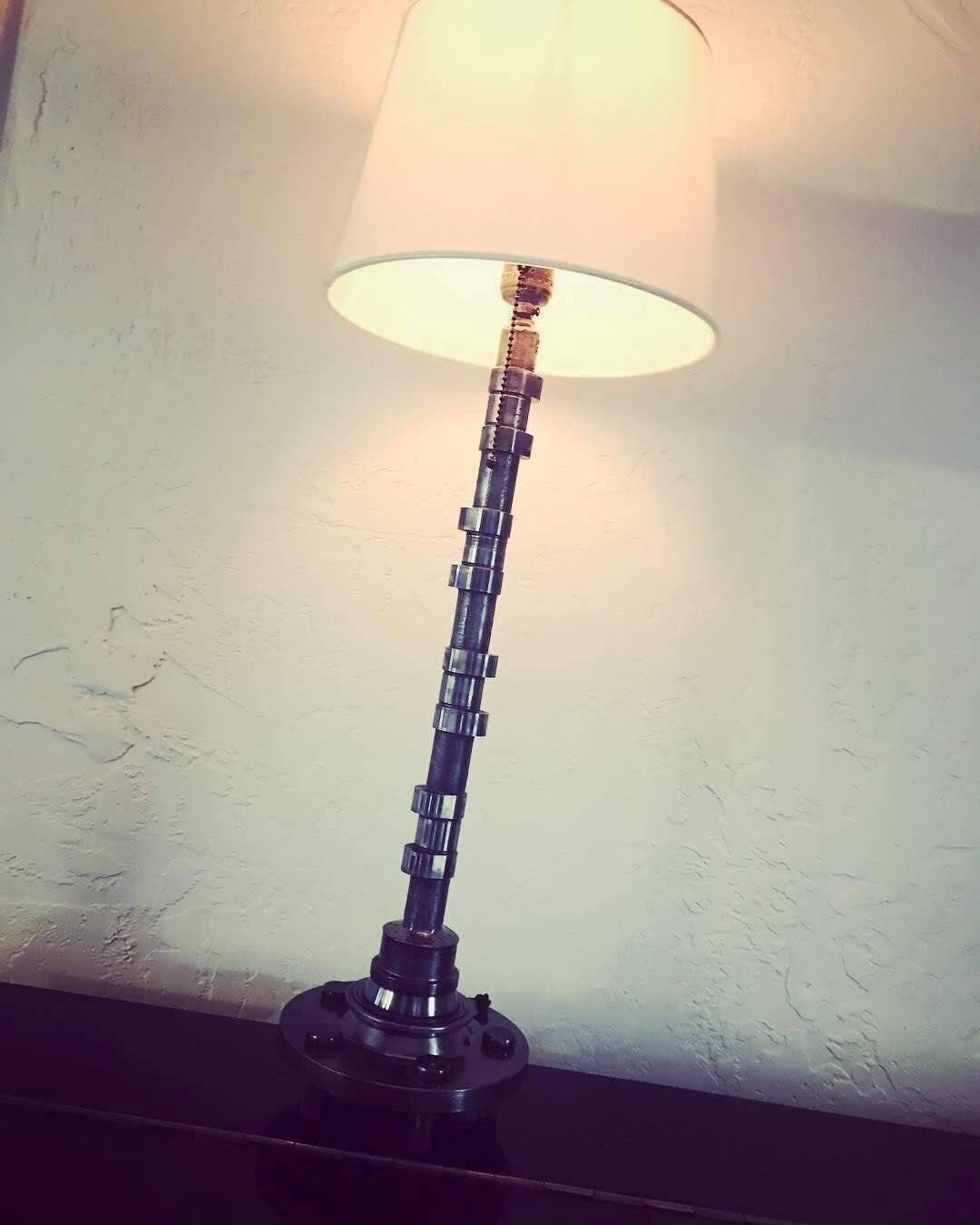 Tabletop lamp handcrafted from a genuine polished car engine camshaft with a LED lightbulb and white shade.