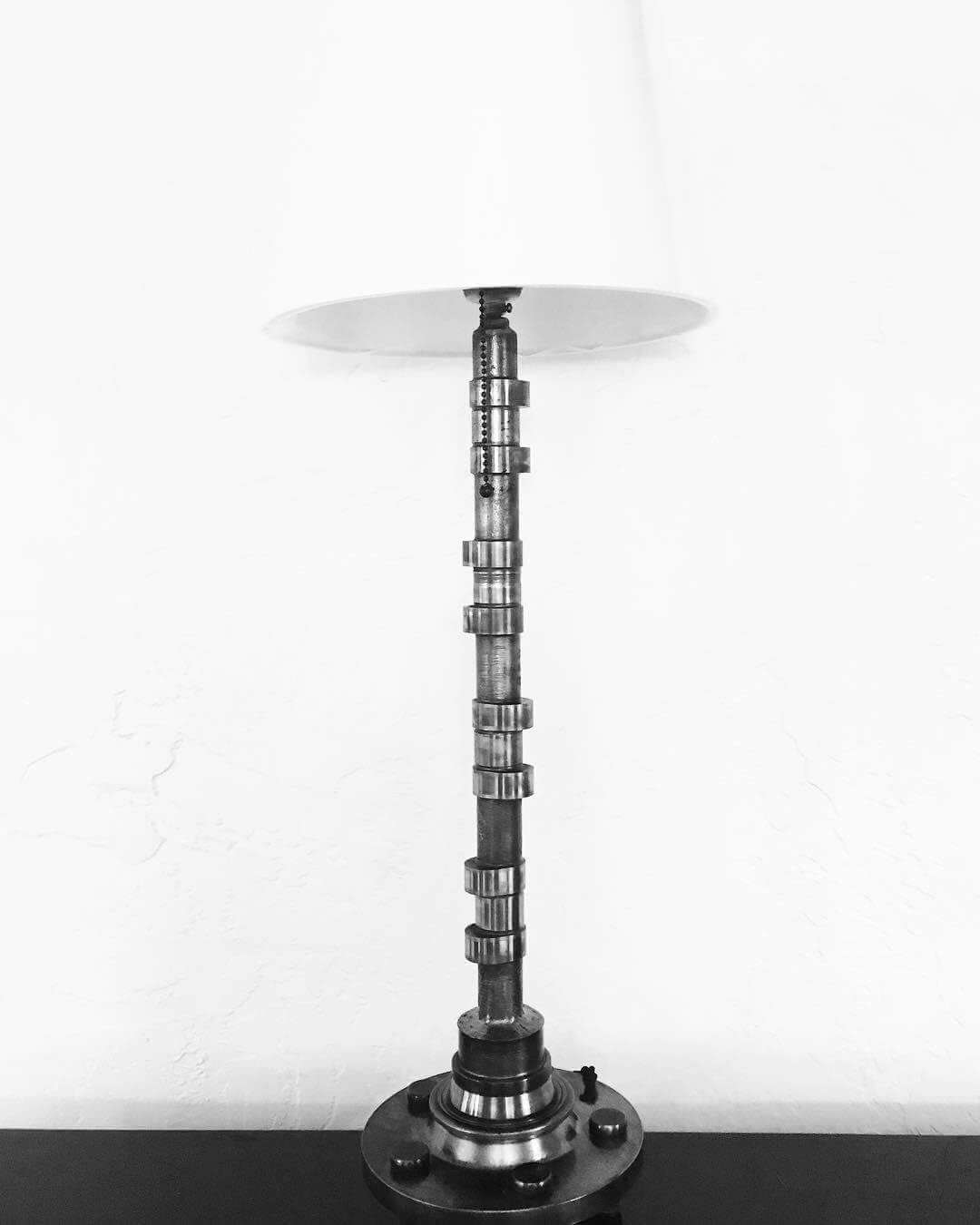Tabletop lamp handcrafted from a genuine polished car engine camshaft with a LED lightbulb and white shade.