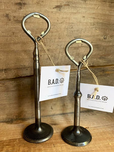 Two bottle openers made out of car engine valves with tags reading, "B.A.D., Ben's Automotive Decor"