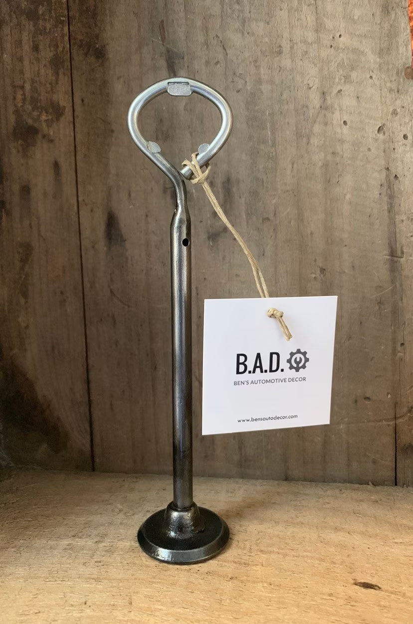 Bottle opener made out of a car engine valve with a tag reading, "B.A.D., Ben's Automotive Decor"