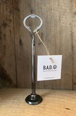 Load image into Gallery viewer, Bottle opener made out of a car engine valve with a tag reading, &quot;B.A.D., Ben&#39;s Automotive Decor&quot;
