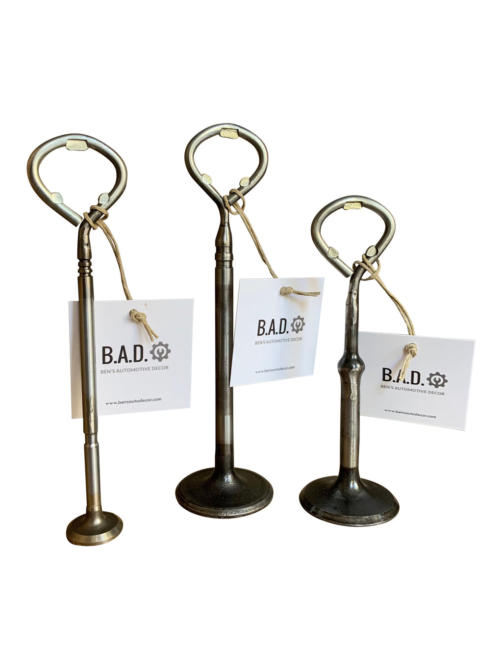 Three bottle openers made out of car engine valves with tags reading, "B.A.D., Ben's Automotive Decor"