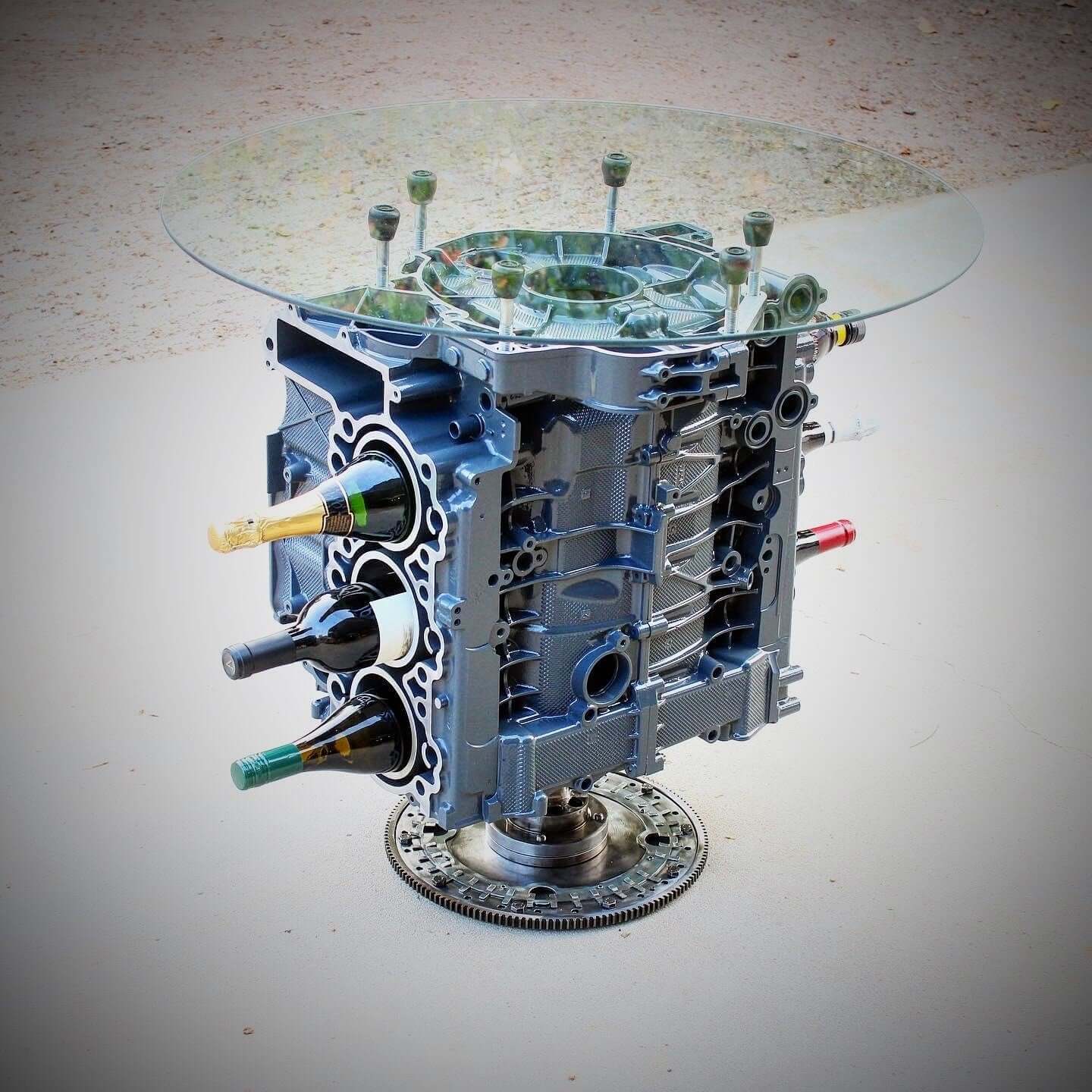 Wine rack table handcrafted from a genuine Porsche car engine, finished in gray and silver with a circular glass top.
