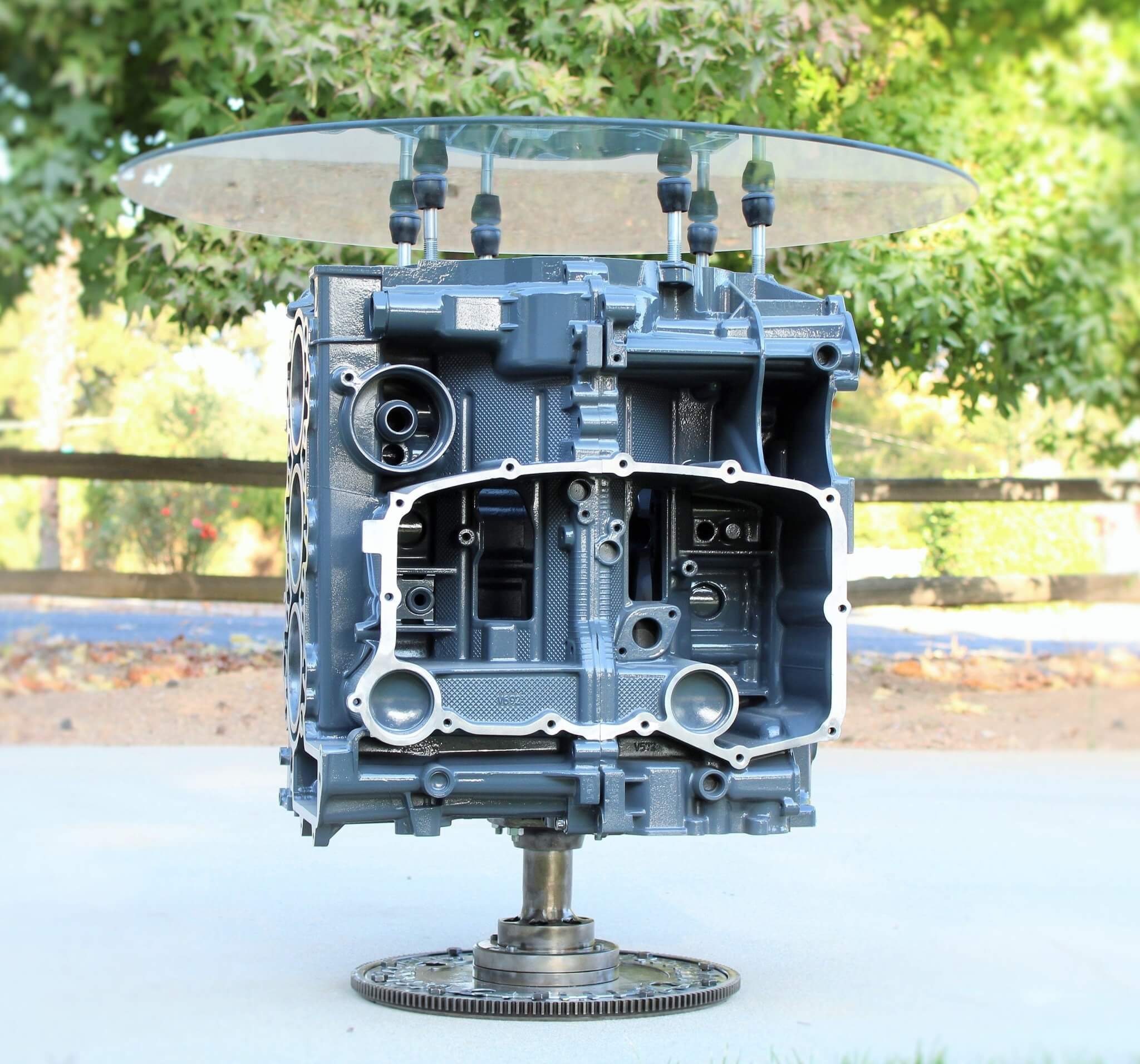 Wine rack table handcrafted from a genuine Porsche car engine, finished in gray and silver with a circular glass top.