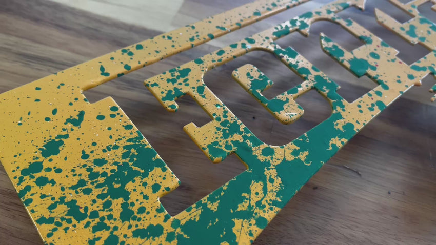 Video of a metal wall art piece of the Ferrari prancing horse logo, hand painted in yellow with green, white and red splatters.