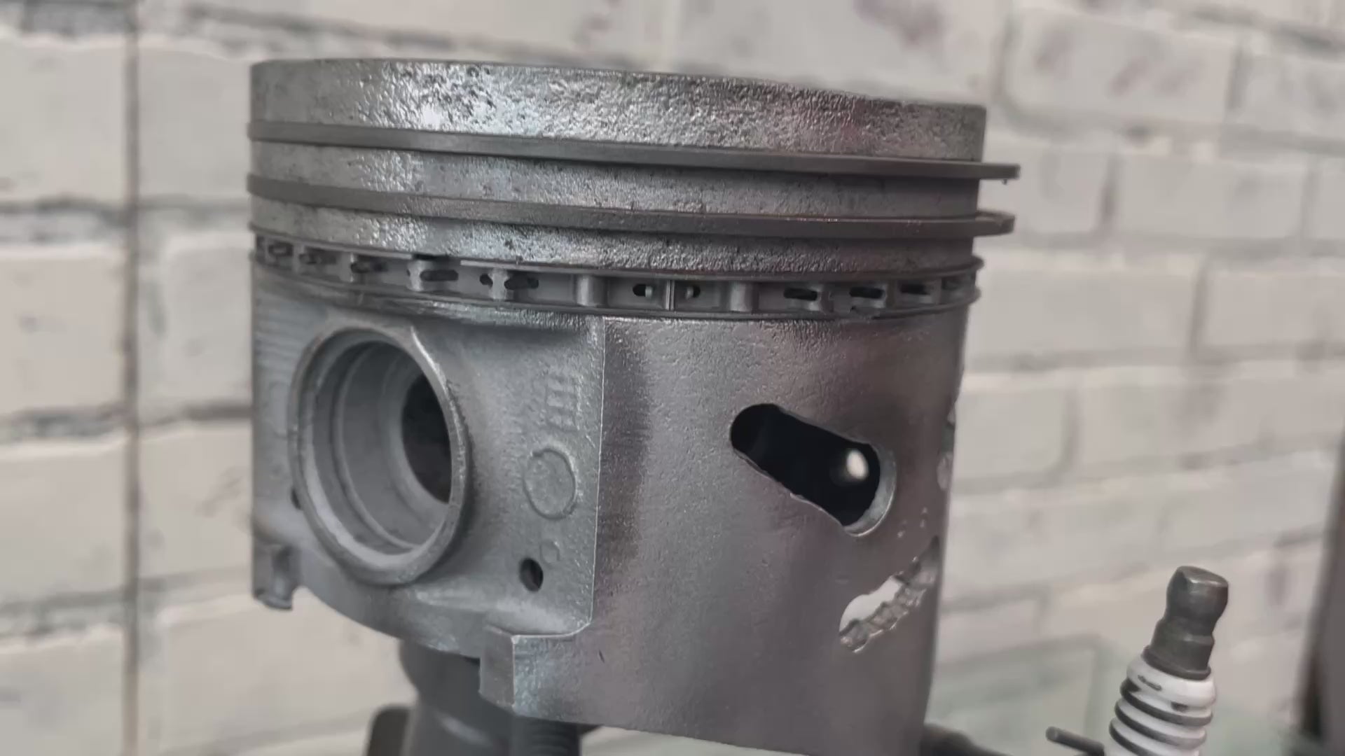 Video of a standing piston man car part sculpture holding a spark plug.