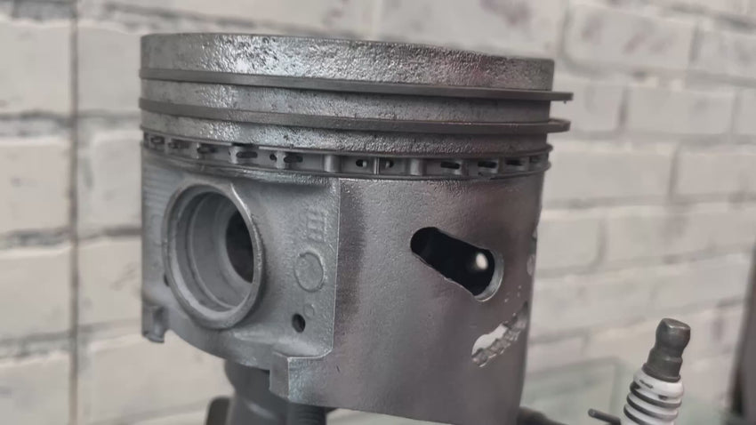 Video of a standing piston man car part sculpture holding a spark plug.
