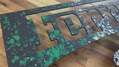 Video of a metal wall art piece of the Ferrari prancing horse logo, hand painted in black with green, white and red splatters.