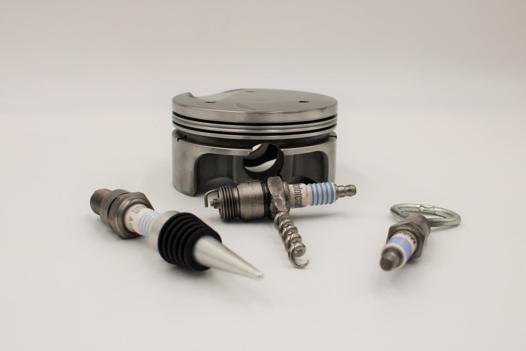 Barware set handcrafted from genuine car engine components - a polished car engine piston holder with a bottle opener, corkscrew, and stopper made from spark plugs.
