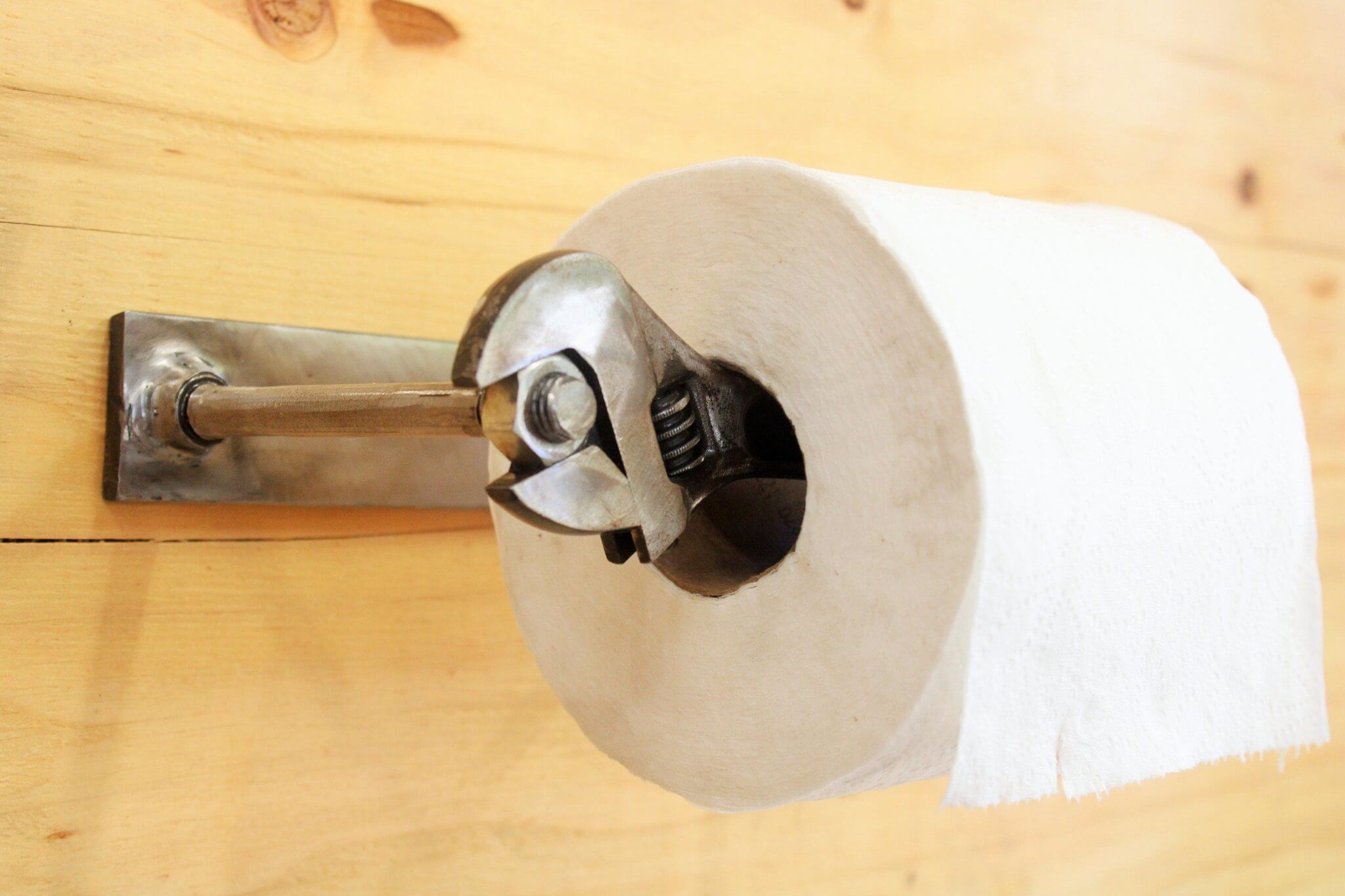 Roll of toilet paper resting on a holder handcrafted from a real wrench with a polished finish and unique restocking mechanism.