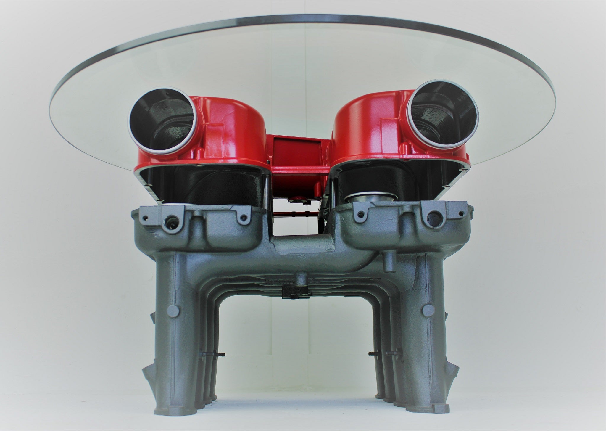 Red and gunmetal grey engine block coffee table with a round glass top.