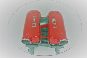 Birds-eye view of a Ferrari intake manifold table, finished in red and gunmetal gray with a round glass top. The Ferrari logo is displayed on both sides.