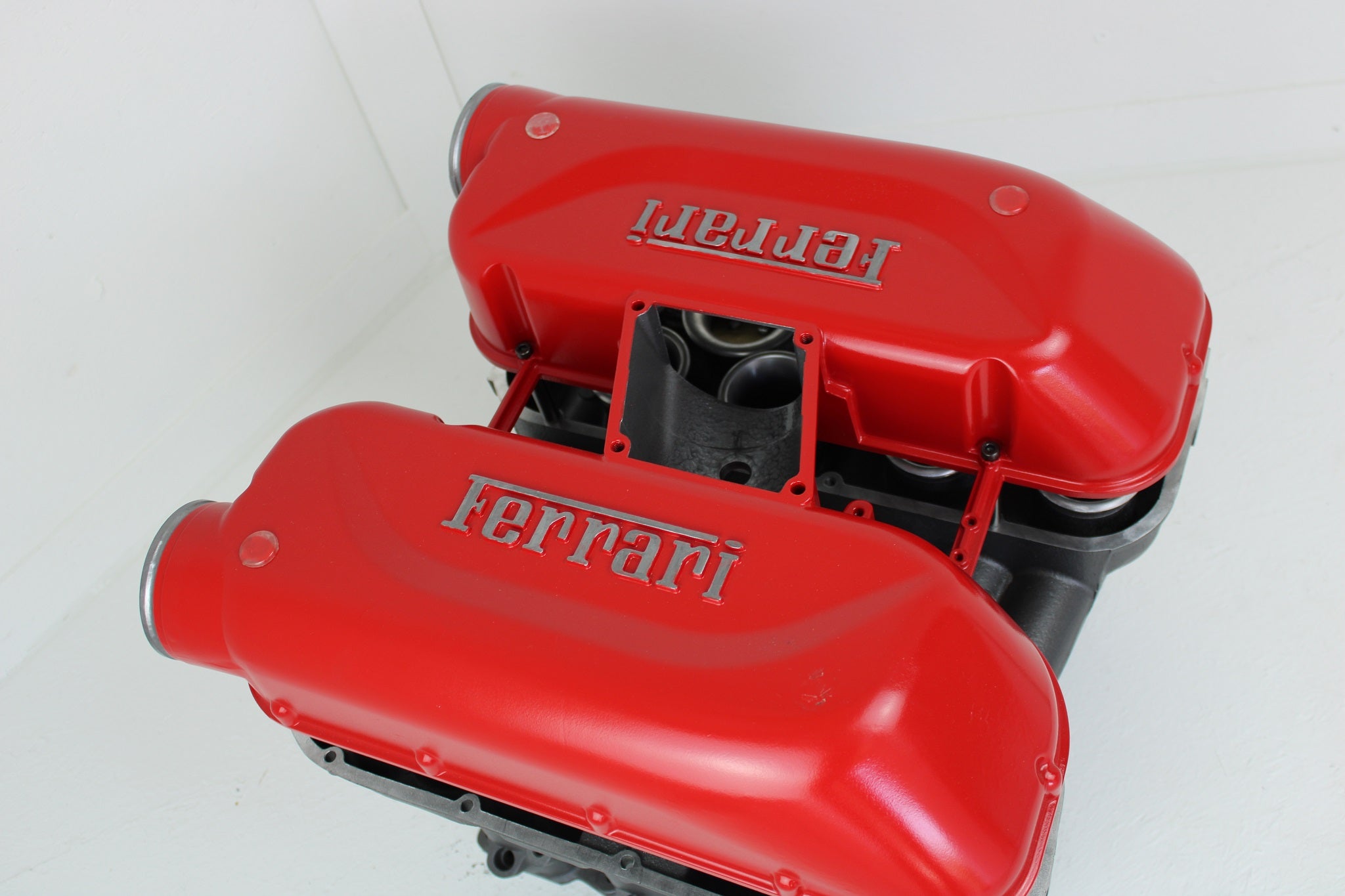 Birds-eye view of a Ferrari intake manifold table without its glass top, finished in red with the Ferrari logo displayed on both sides.
