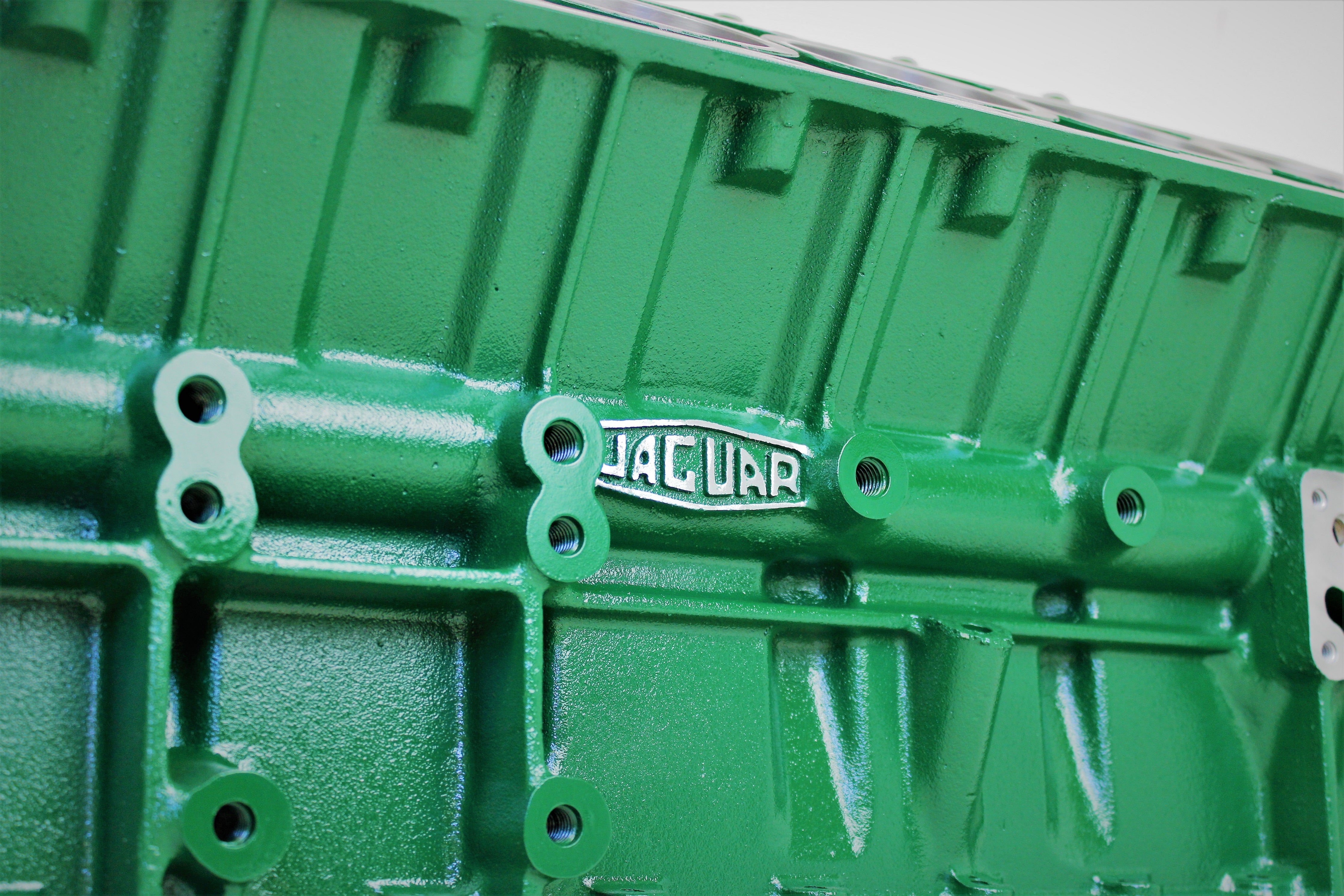 Close-up view of a Jaguar V12 engine block coffee table finished in British Racing Green and the Jaguar logo displayed in the center.
