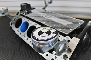 A close-up of the BMW logo on a BMW M Series V10 engine block coffee table painted in the BMW M-Power color scheme without its glass top, the M-Power logo displayed across the piece, and the BMW logo on each of the four car pistons.