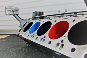 A close-up side view of a BMW M Series V10 engine block coffee table painted in the BMW M-Power color scheme without its glass top.