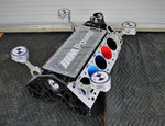 Load image into Gallery viewer, BMW M Series V10 engine block coffee table painted in the BMW M-Power color scheme without its glass top, the M-Power logo displayed across the piece, and the BMW logo etched into each of the four car pistons.

