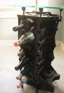 Engine block wine rack finished in black with a square glass top, bottles stored in its side.