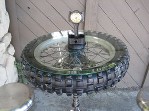 Pub table made from a tire and crankshaft, with two stools by its side and a clock made from a car piston on top.