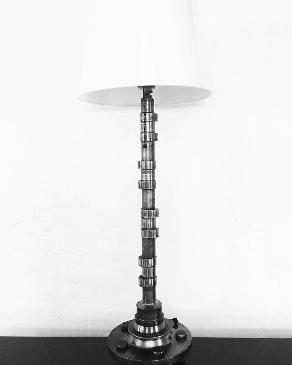 Silver lamp made out of a car's camshaft with its shade.