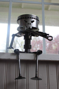 Piston man car part sculpture sitting on a windowsill and holding a wrench.