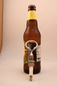 Bottle opener made from a car's spark plug resting against a bottle of beer.