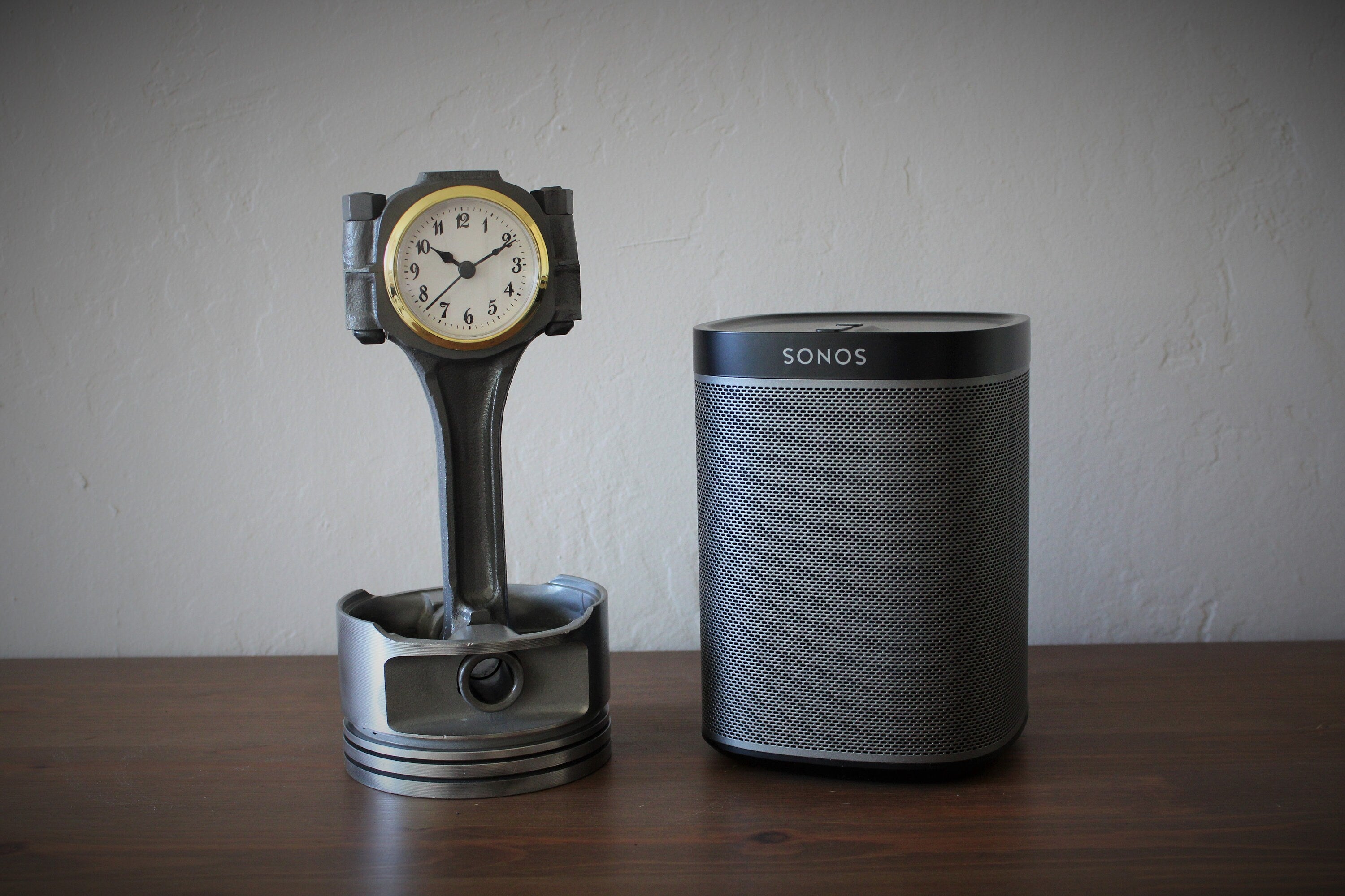 Clock made from a Chevrolet car's piston with a gold clock ring on a table next to a speaker.