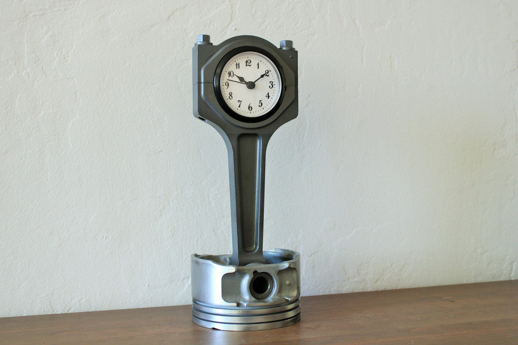 A piston clock made from a Jaguar car's piston, finished in gunmetal gray.