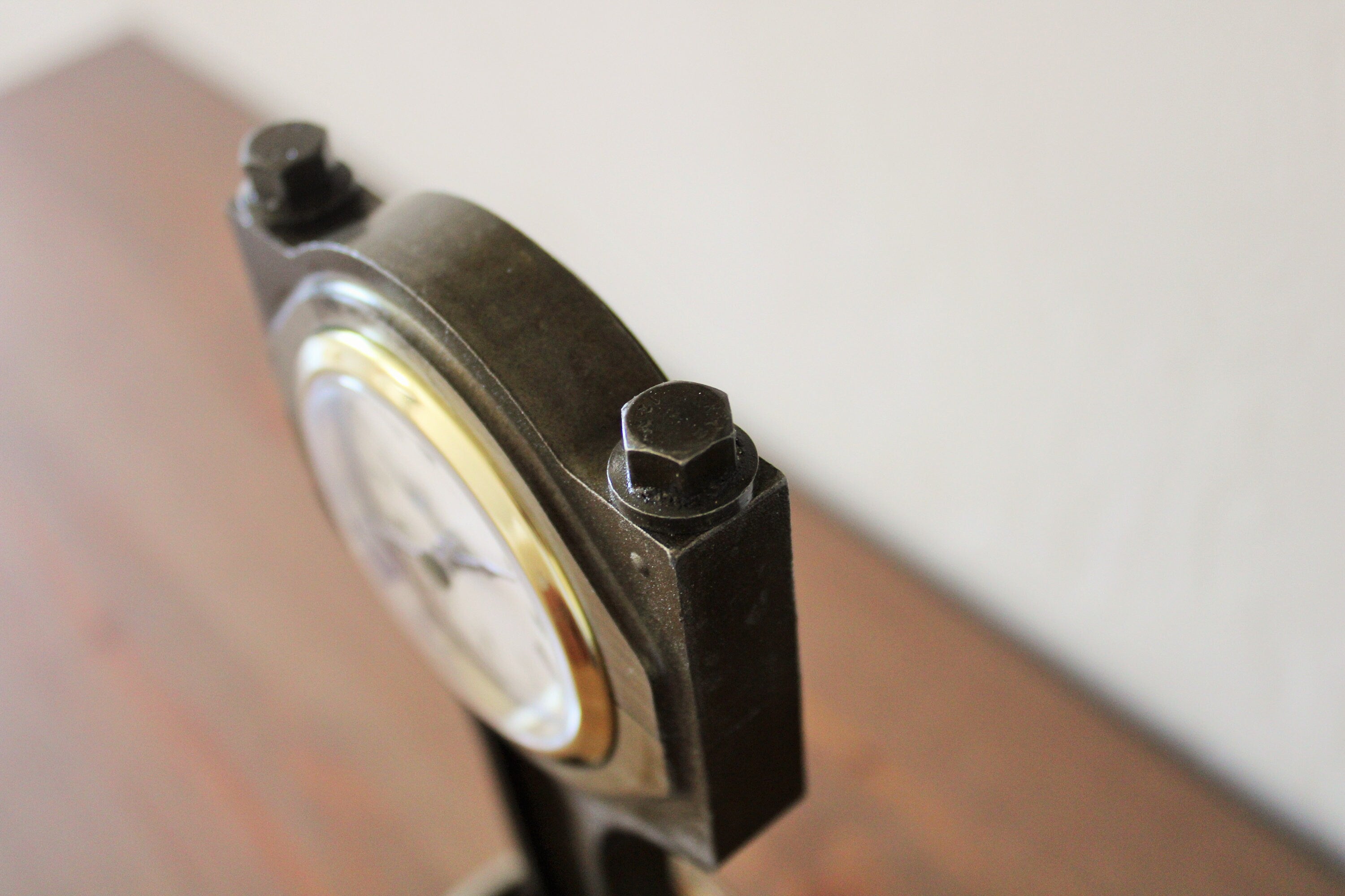 Close-up view of a piston clock made out of a Jaguar car's piston with a patina finish and gold clock ring.