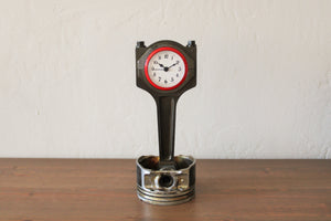 A piston clock made out of a Jaguar car's piston with a red clock ring and patina finish.