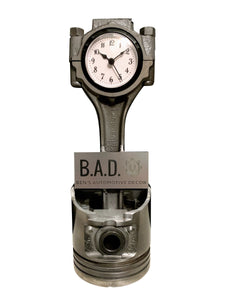 A piston clock finished in gunmetal gray that includes a custom engraved plaque that reads, "B.A.D, Ben's Automotive Decor".