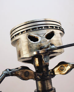 Close-up view of a piston man car part sculpture holding a wrench.