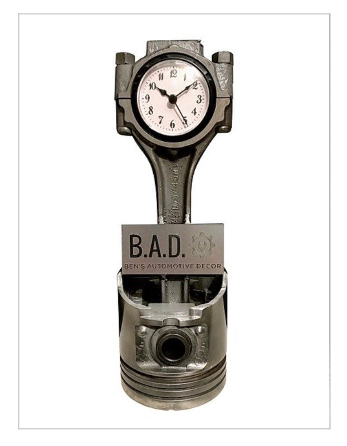 A clock made from a car engine's piston displaying a custom engraved plaque that reads, "B.A.D., Ben's Automotive Decor"