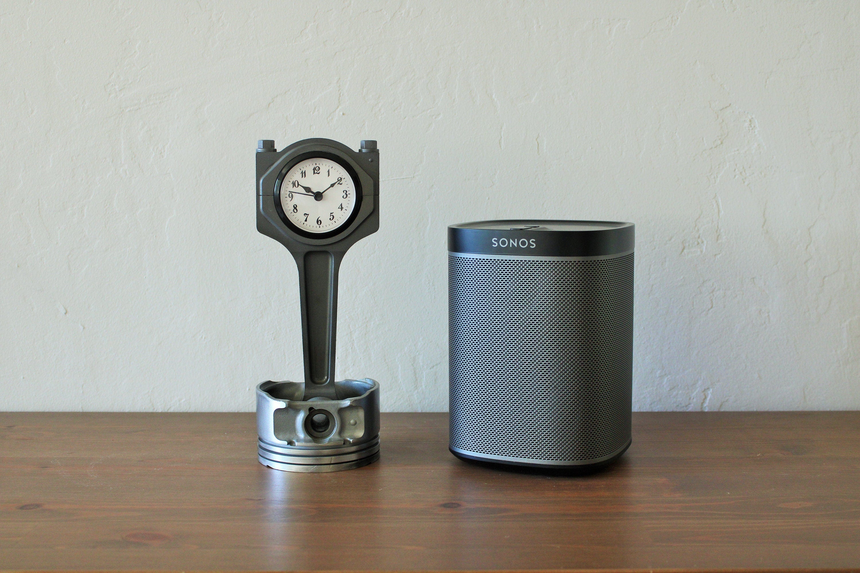 A piston clock made out of a Jaguar car's piston finished in gunmetal gray next to a speaker.