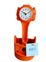 Load image into Gallery viewer, A piston clock finished in bright orange with a tag reading, &quot;B.A.D., Ben&#39;s Automotive Decor&quot;.
