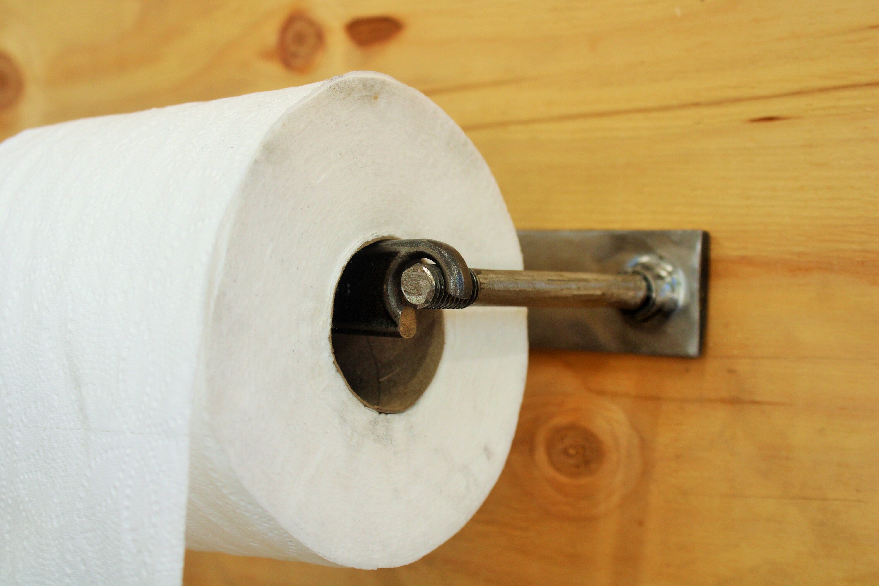 Close-up view of the wrench and nut toilet paper holder with a roll of toilet paper on it.