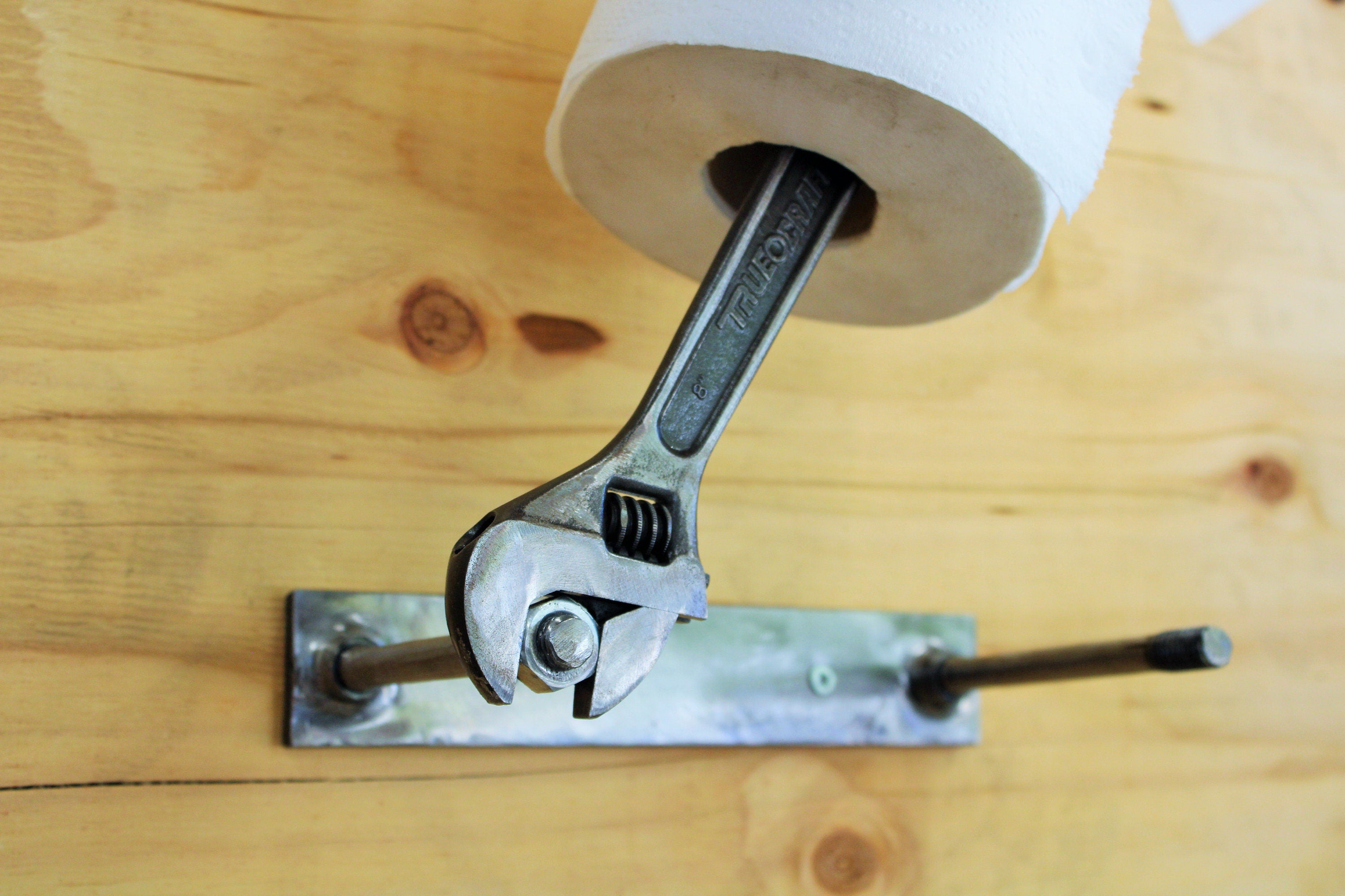 Wrench and nut toilet paper holder being turned to change its toilet paper roll.