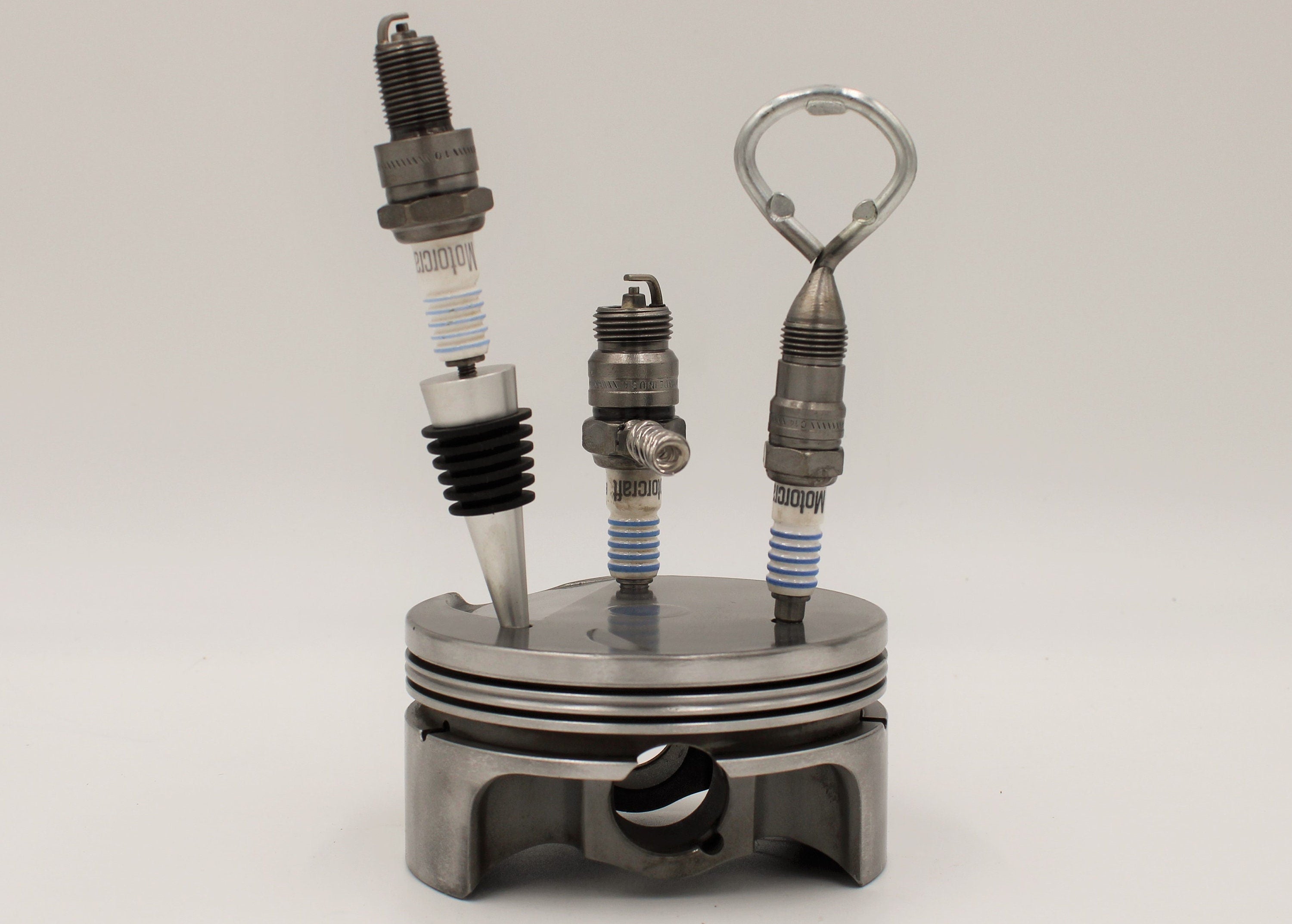 Spark plug bar set including a wine stopper, corkscrew and bottle opener, all made from car spark plugs and in a car piston holder.